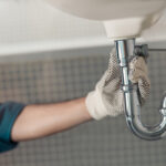 Handyman is repairing faucet of a sink at bathroom. Maintenance and household assistance concept